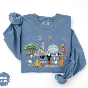 A blue long-sleeved t-shirt with a graphic design depicting Disney characters and landmarks, including Mickey Mouse, Goofy, Donald Duck, and the Eiffel Tower.