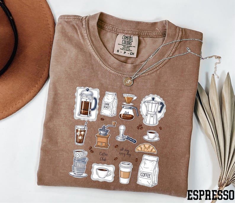 a brown t-shirt with a graphic design depicting various coffee-related items such as a coffee maker, coffee cup, and coffee beans.