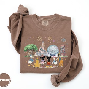 A brown t-shirt with a printed design depicting Disney characters and landmarks, including Mickey Mouse, Donald Duck, Goofy, and Eiffel Tower.
