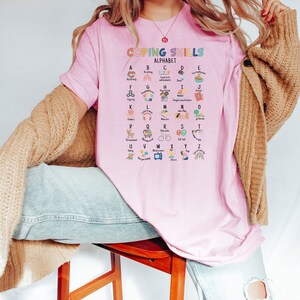 May include: Pink t-shirt with the text "Coping Skills Alphabet" and a colorful alphabet chart with coping skills for each letter.