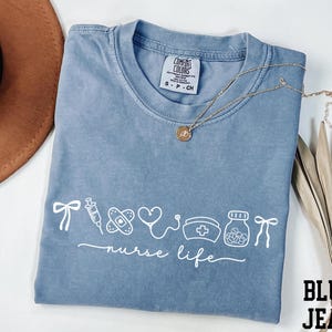 a blue t-shirt with white text and graphics, a brown hat, and some dried leaves, all arranged on a white background.