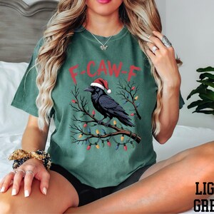 A woman wearing a green t-shirt with a graphic of a bird wearing a Santa hat and Christmas lights.