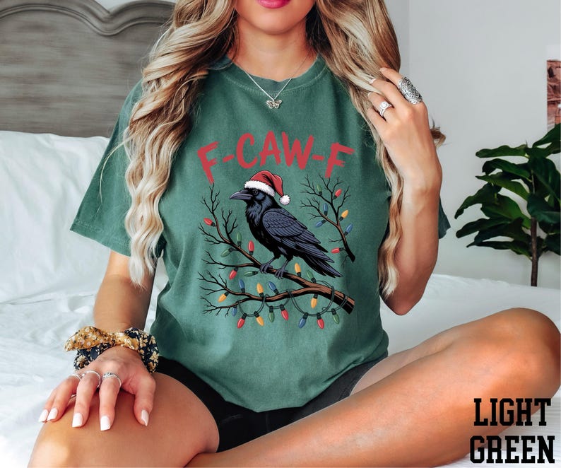 A woman wearing a green t-shirt with a graphic of a bird wearing a Santa hat and Christmas lights.