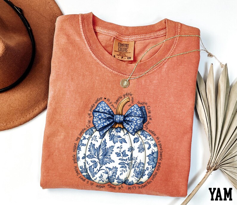 a red t-shirt with a blue and white floral pumpkin design, a brown hat, and a fan, all arranged on a white background.