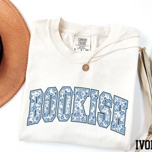 a white t-shirt with the word "BOOKISH" printed on it, along with a brown hat and a necklace.