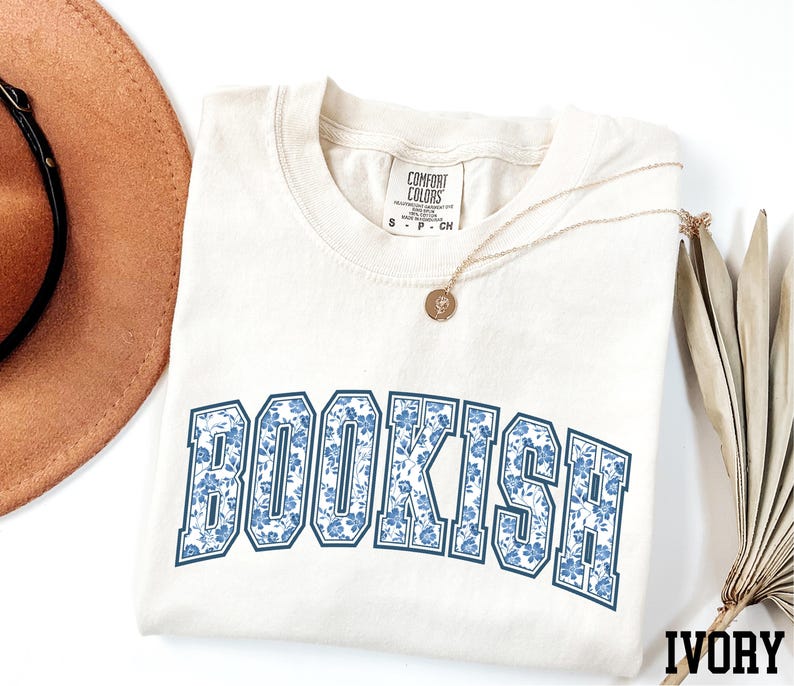 a white t-shirt with the word "BOOKISH" printed on it, along with a brown hat and a necklace.