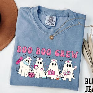 A blue t-shirt with a graphic design featuring five ghost characters dressed as nurses, along with the text "BOO BOO CREW".