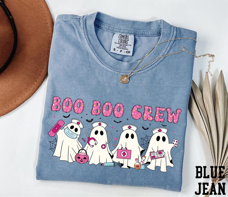 A blue t-shirt with a graphic design featuring five ghost characters dressed as nurses, along with the text "BOO BOO CREW".