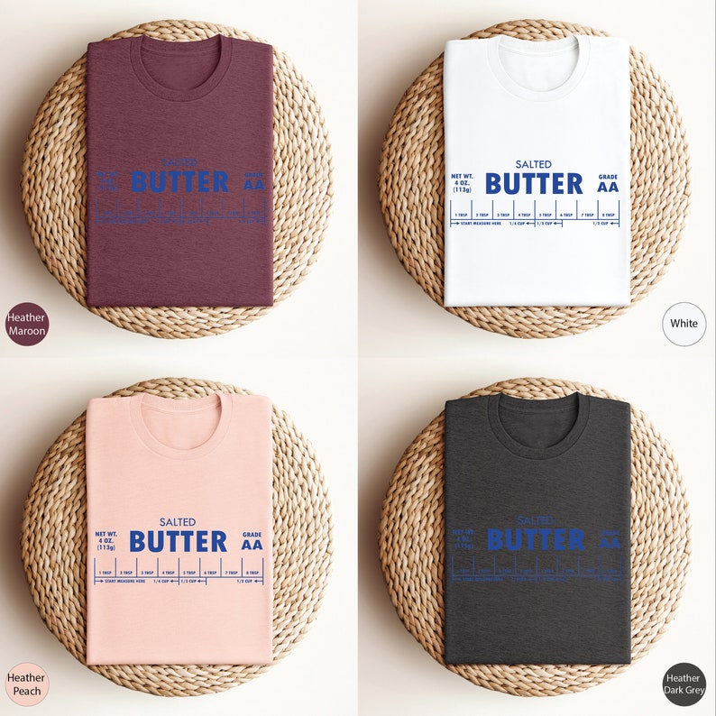 Puede incluir: Cuatro camisetas de diferentes colores, Heather Marr&oacute;n, Blanco, Heather Melocot&oacute;n y Heather Gris Oscuro, con un gr&aacute;fico de una barra de mantequilla con el texto "SALTED BUTTER AA" y una tabla que muestra el peso neto y la calidad de la mantequilla.