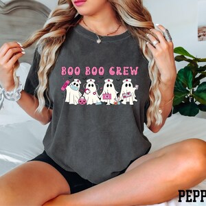 A woman wearing a black t-shirt with a graphic design of five ghost characters and the text "BOO BOO CREW" printed on it.