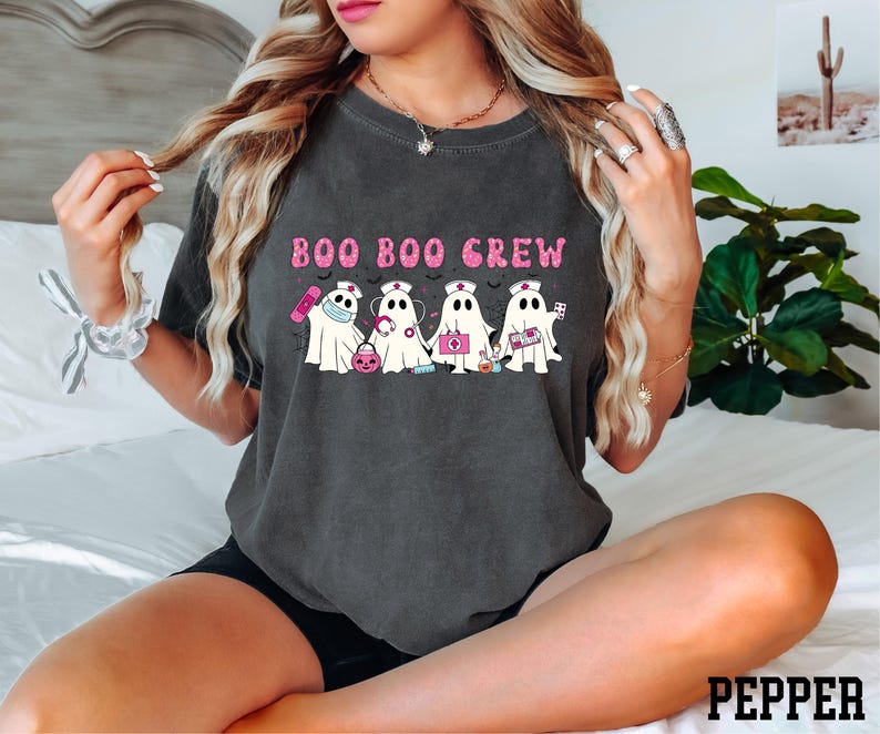 A woman wearing a black t-shirt with a graphic design of five ghost characters and the text "BOO BOO CREW" printed on it.