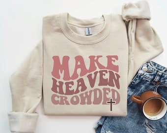 May include: A beige sweatshirt with a pink and red gradient graphic that says "Make Heaven Crowded" with a brown cross underneath.