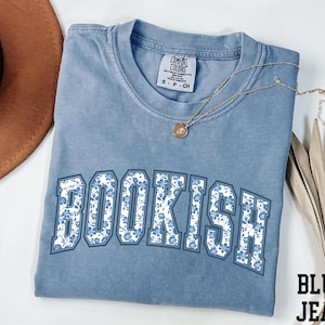 a blue t-shirt with the word "BOOKISH" printed on it, along with a brown hat and some leaves.