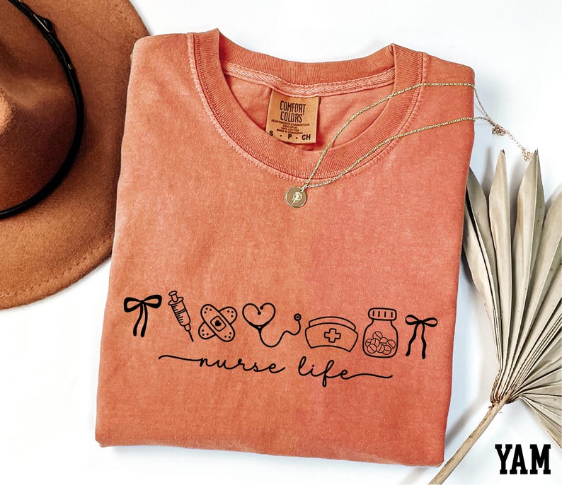 a pink t-shirt with a graphic design, a brown hat, a necklace, and a fan, all arranged on a white background.