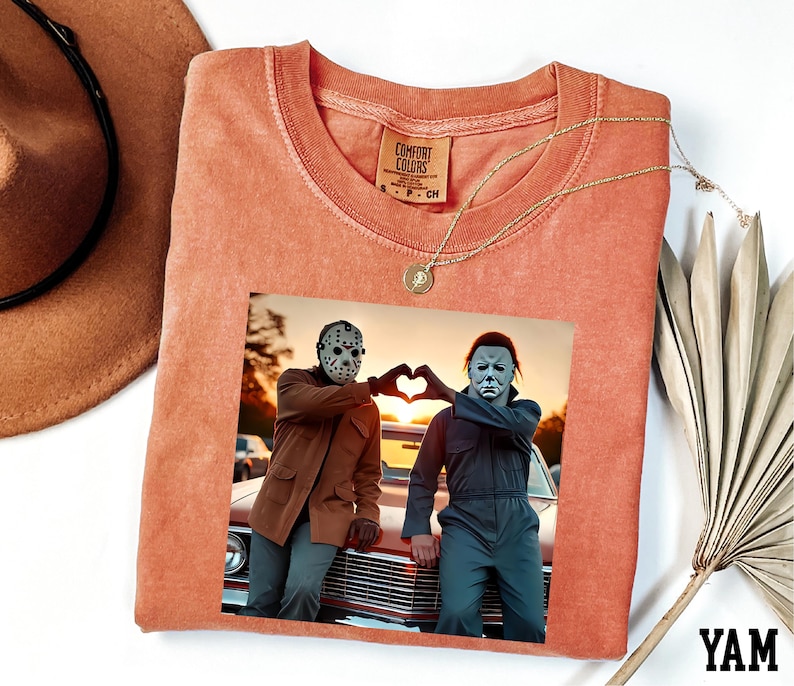 a t-shirt with a printed photo of two people posing with their hands in a heart shape, along with a necklace and a hat.