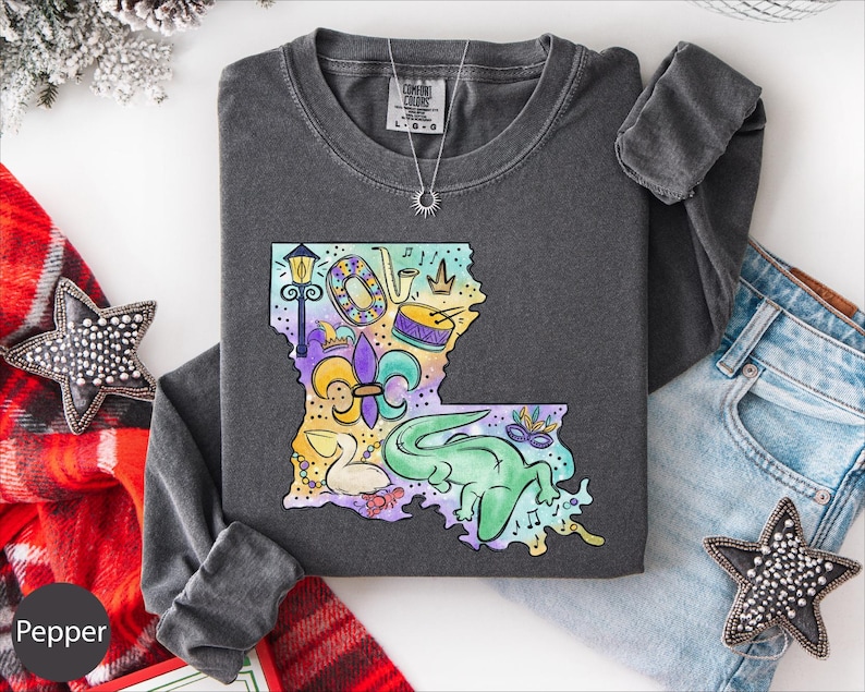 a gray long-sleeved shirt with a colorful, whimsical design of a map of Louisiana, surrounded by various decorative items such as a star, a scarf, and a necklace.