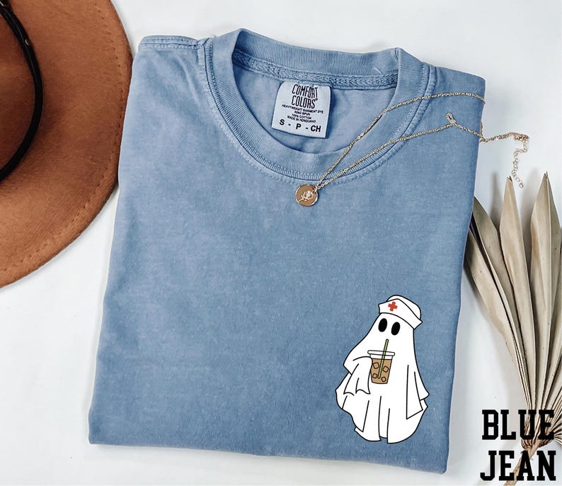 a blue t-shirt with a ghost wearing a nurse's outfit and holding a coffee cup, along with a brown hat and some leaves.