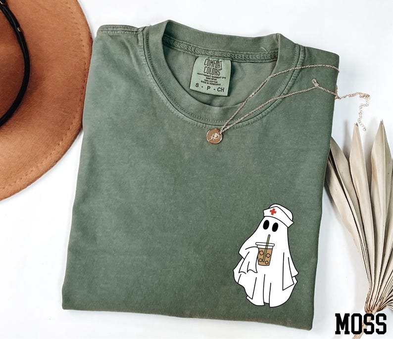a green t-shirt with a cartoon ghost wearing a nurse's hat, along with a brown hat, a necklace, and some dried leaves.