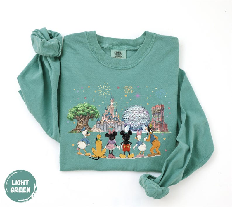 A green long-sleeved t-shirt with a printed design depicting Disney characters and landmarks, including Mickey Mouse, Donald Duck, Goofy, and Eiffel Tower.