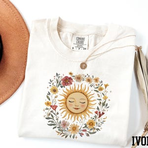 a white t-shirt with a sun design, a brown hat, and a necklace, all arranged on a white background.