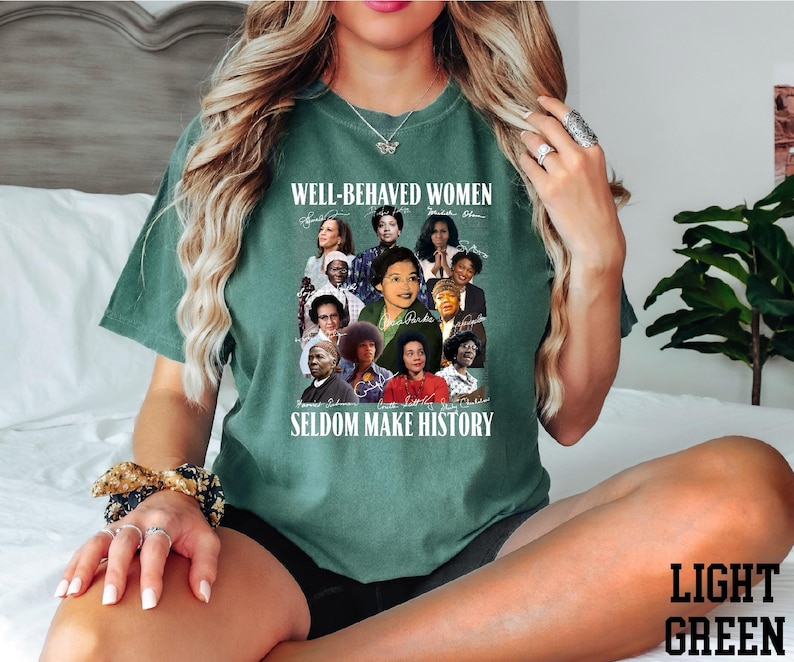 A woman wearing a green t-shirt with a collage of diverse women's portraits and the text "WELL-BEHAVIED WOMEN" printed on it.