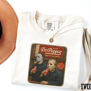 a white t-shirt with a graphic design depicting two men wearing masks, one holding a can of Dr. Pepper.