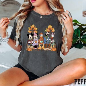 A woman wearing a t-shirt with a graphic of Disney characters is sitting on a bed.