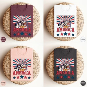 May include: Four t-shirts with a graphic of Mickey Mouse, Donald Duck, Goofy, and Pluto wearing red, white, and blue patriotic clothing. The shirts are available in Heather Maroon, White, Heather Peach, and Heather Dark Grey.