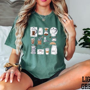 A woman wearing a green t-shirt with various coffee-related icons and illustrations, including coffee cups, coffee machines, and other related items.
