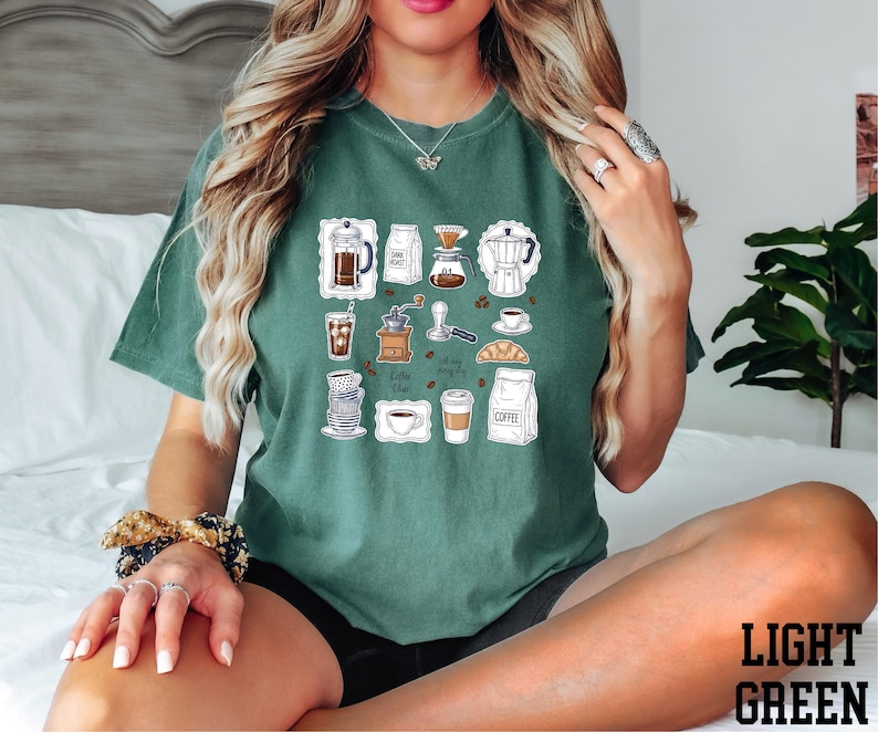 A woman wearing a green t-shirt with various coffee-related icons and illustrations, including coffee cups, coffee machines, and other related items.
