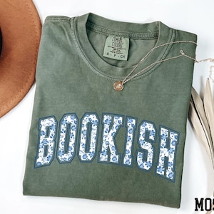 a green t-shirt with the word "BOOKISH" printed on it, along with a brown hat and some dried leaves.