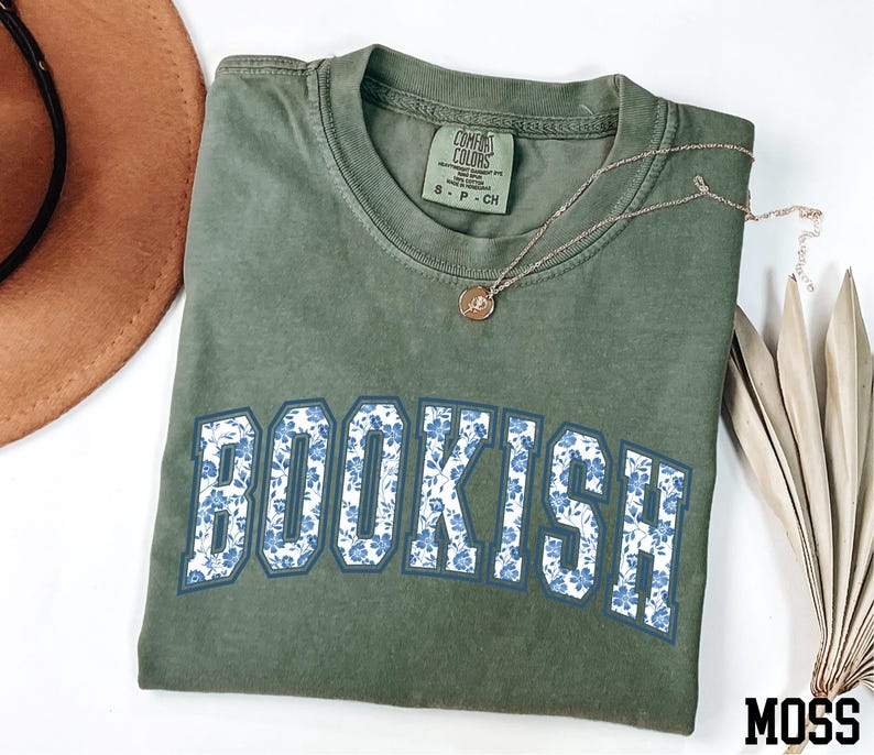 a green t-shirt with the word "BOOKISH" printed on it, along with a brown hat and some dried leaves.