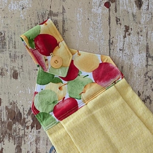 May include: A yellow kitchen towel with a hanging loop. The loop is made of white fabric with a red, yellow, and green apple print.
