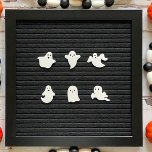 May include: A black letter board with six white ghost shapes arranged in two rows. The letter board is framed in black and has a black felt surface.