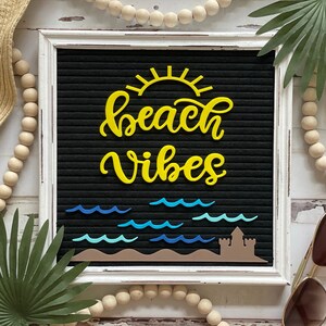 May include: A white framed letter board with a black felt background. The board has yellow felt letters spelling out "beach vibes" with a yellow sun above the text. Blue felt waves are below the text.