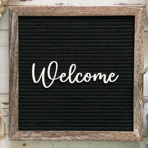 May include: A black letter board with a wooden frame, displaying the word "Welcome" in white letters.