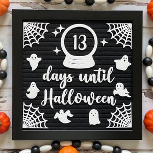 May include: A black letter board with white letters spelling "13 days until Halloween". The board is decorated with white paper cutouts of ghosts, stars, and spiderwebs.