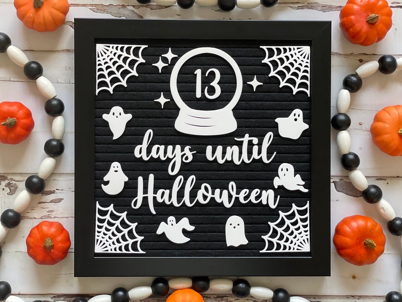 May include: A black letter board with white letters spelling "13 days until Halloween". The board is decorated with white paper cutouts of ghosts, stars, and spiderwebs.