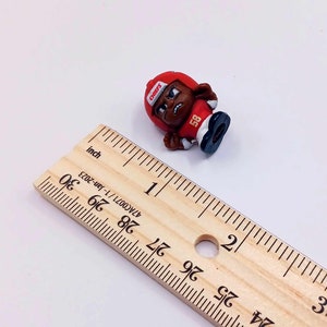 May include: A small red and black plastic figurine of a football player wearing a helmet with the word "CHIEFS" on it. The player is wearing a jersey with the number "58" on it. The figurine is about 1 inch tall.