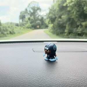 May include: A small blue and white figurine of a football player wearing a helmet with the word "TITANS" on it. The figurine is sitting on a black surface.