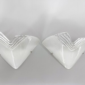 May include: A pair of white glass wall sconces with a geometric design. The sconces have a silver-colored finish and are mounted on a white wall.