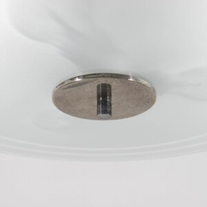 May include: Close-up of a silver ceiling fixture with a round metal plate and a metal rod extending down.