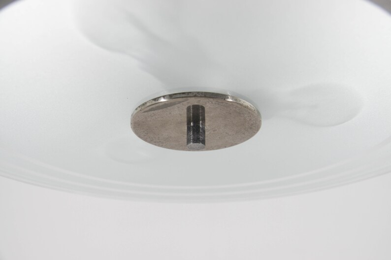 May include: Close-up of a silver ceiling fixture with a round metal plate and a metal rod extending down.
