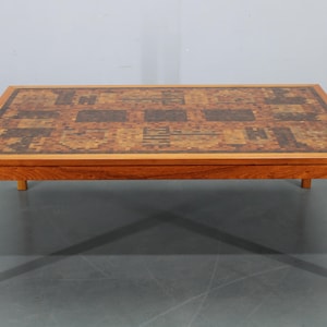 May include: Rectangular wooden coffee table with a mosaic tile top. The table has a warm, reddish-brown hue, with a mosaic pattern in shades of brown, tan, and black. The legs are straight and sturdy. The table measures approximately 48 inches long.