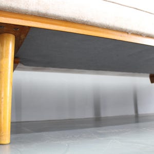 May include: A white fabric sofa with wooden legs. The sofa is on a light gray floor.