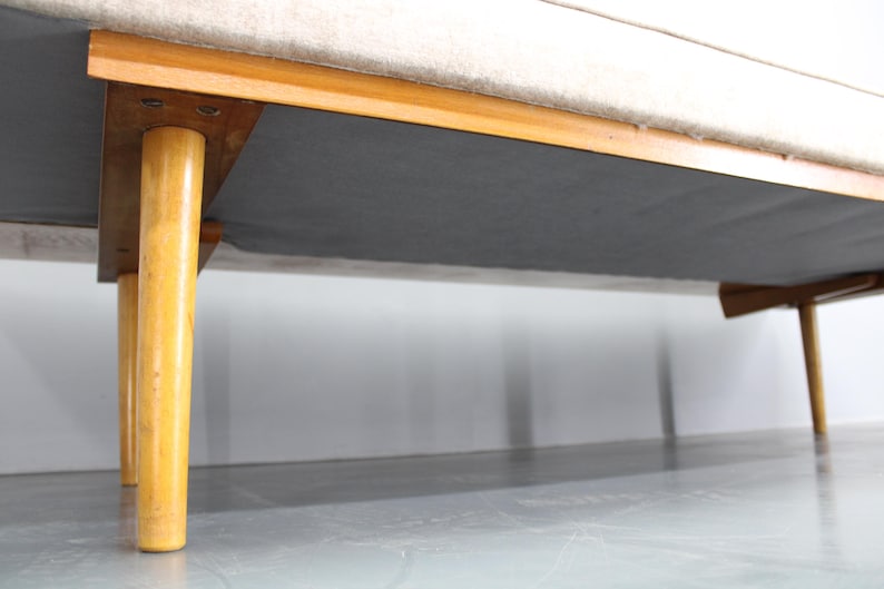 May include: A white fabric sofa with wooden legs. The sofa is on a light gray floor.