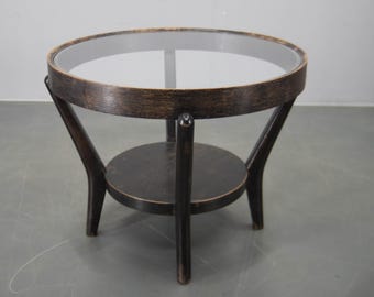 Puede incluir: Una pequeña mesa auxiliar redonda con estructura de madera oscura y tapa de cristal transparente. La mesa tiene un estante inferior y tres patas curvas. Aproximadamente 61 cm de diámetro y 51 cm de altura.