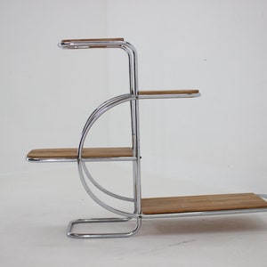 May include: A chrome plant stand with four wooden shelves. The stand has a curved design and is made of polished chrome.