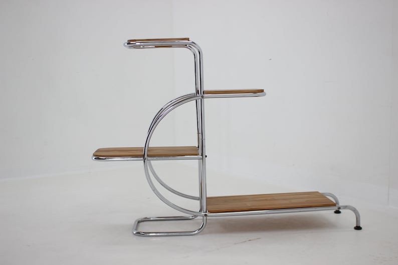 May include: A chrome plant stand with four wooden shelves. The stand has a curved design and is made of polished chrome.
