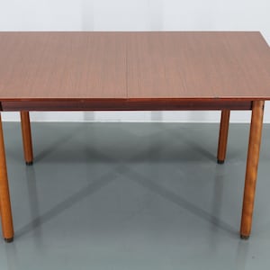 May include: A rectangular wooden table with a brown finish and four legs. The table has a leaf that can be extended to make it longer.